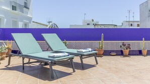 Deux fauteuils de jardin avec des serviettes, une terrasse carrelée, des plantes en pot et un mur bleu.