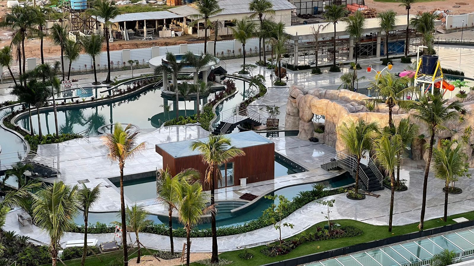 A resort with multiple swimming pools, palm trees, and a central rock formation.