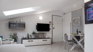 Un salon moderne doté d’un téléviseur à écran plat, d’un coin repas avec une table et des chaises, d’un meuble blanc et d’une plante en pot.