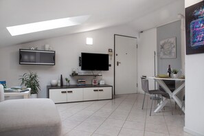 A modern living room with a flat-screen TV, a dining area with a table and chairs, a white cabinet, and a potted plant.