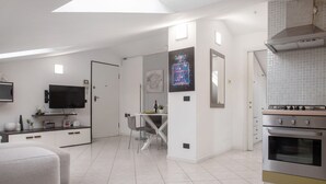 Une cuisine moderne dotée d’un four encastré, un coin repas avec une table et des chaises, et un téléviseur posé sur un meuble.
