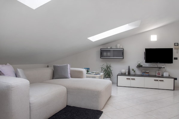A modern living room with a sectional sofa, a flat-screen TV, a small side table, and a potted plant.