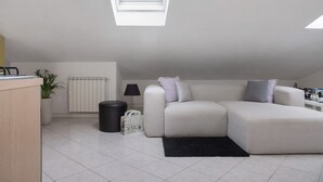 Un salon moderne avec un canapé d’angle, un tapis noir, une plante en pot, une lampe et un radiateur.
