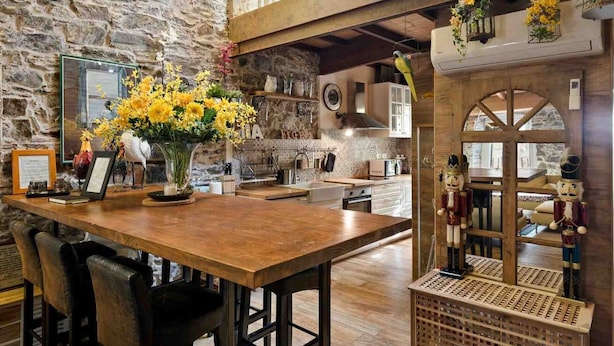 A rustic kitchen with a wooden table, chairs, and a vase of yellow flowers. There are nutcracker figurines and a birdcage with flowers on the wall. - My Home, Welcome Way (Riomaggiore)