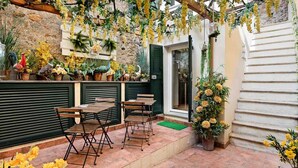 An outdoor patio with wooden tables and chairs, surrounded by potted plants and flowers. - My Home, Welcome Way (Riomaggiore)