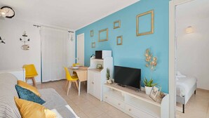 A compact room with a bed, a desk with a computer, a TV, and a small plant. - The Echo in the Rock, Welcome Way (Vernazza)