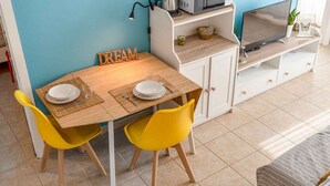 A dining area with a wooden table, two yellow chairs, a white cabinet, and a TV on a stand. - The Echo in the Rock, Welcome Way (Vernazza)