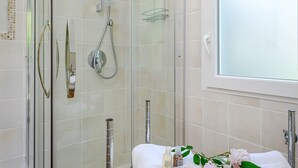 Un baño moderno con ducha de vidrio, una bañera blanca y un ventanal que proporciona luz natural.