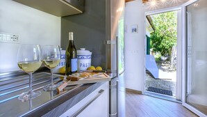 Una cocina con dos copas de vino, una botella, una tabla de cortar con un cuchillo y un recipiente con pasta.
