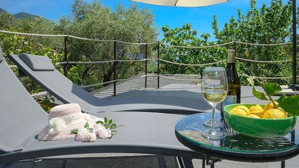 Un espacio al aire libre iluminado por el sol, con sillones de lounge, una mesa con una copa de vino blanco, un cuenco de limones y un sombrero adornado con flores.