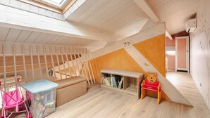 Un plafond en pente avec un puits de lumière, un banc en bois, un banc avec rangement intégré, une petite table et une chaise pour enfant, le tout dans une pièce dont le sol est recouvert de planches de bois.