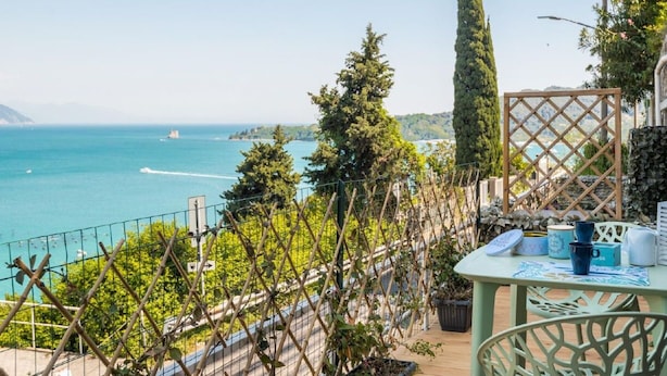 Ein Balkon mit Meerblick, ein Tisch mit Gegenständen und eine Rankgitterkonstruktion mit Pflanzen.
