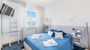 Ein ordentlich eingerichtetes Hotelzimmer mit Bett, Fernseher, einer Hockerleiter und Blick ins Freie.