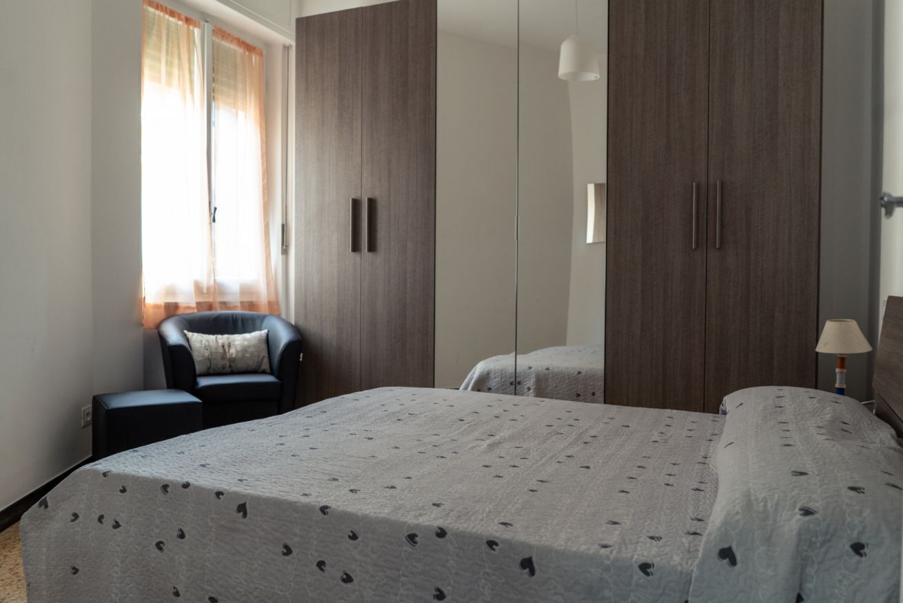 A bedroom with a bed, a chair, a wardrobe, and a bedside table.