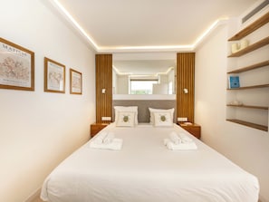 Une chambre d’hôtel moderne, dotée d’un grand lit, de tables de chevet, d’un miroir et d’œuvres d’art encadrées accrochées aux murs.