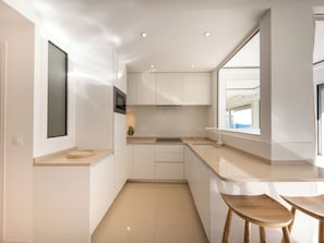 Cozinha moderna com armários brancos, micro-ondas embutido, uma janela ampla e um pequeno espaço de jantar com banquetas.