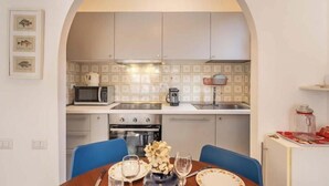 A compact kitchen with a microwave, coffee maker, and oven. There is a dining table with chairs and a vase of flowers.