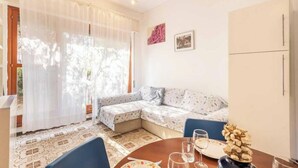 A room with a sofa, a dining table with chairs, a cabinet, and a window with sheer curtains.