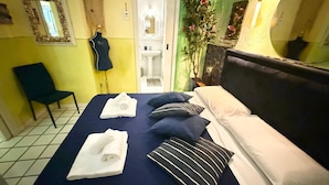 Hotellihuone, jossa on sänky, tuoli, peili ja kylpyhuone, joka näkyy avoimesta ovesta.