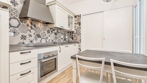 A modern kitchen with white cabinets, a built-in oven, a grey countertop, and a patterned backsplash. - Queen of Sea Diamond, Terre Marine (Manarola)