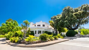 A white building with a sign reading 'RECEPCAO' surrounded by lush greenery and a clear blue sky.