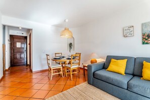 Uma sala de estar com sofá, mesa de jantar com cadeiras, luminária pendente e uma porta.