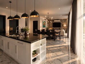 A modern kitchen with a central island, pendant lighting, and a dining area with a TV mounted on the wall.