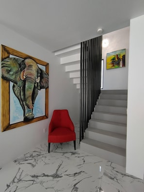 Un interior moderno con una escalera, una silla roja y un cuadro de un elefante enmarcado.
