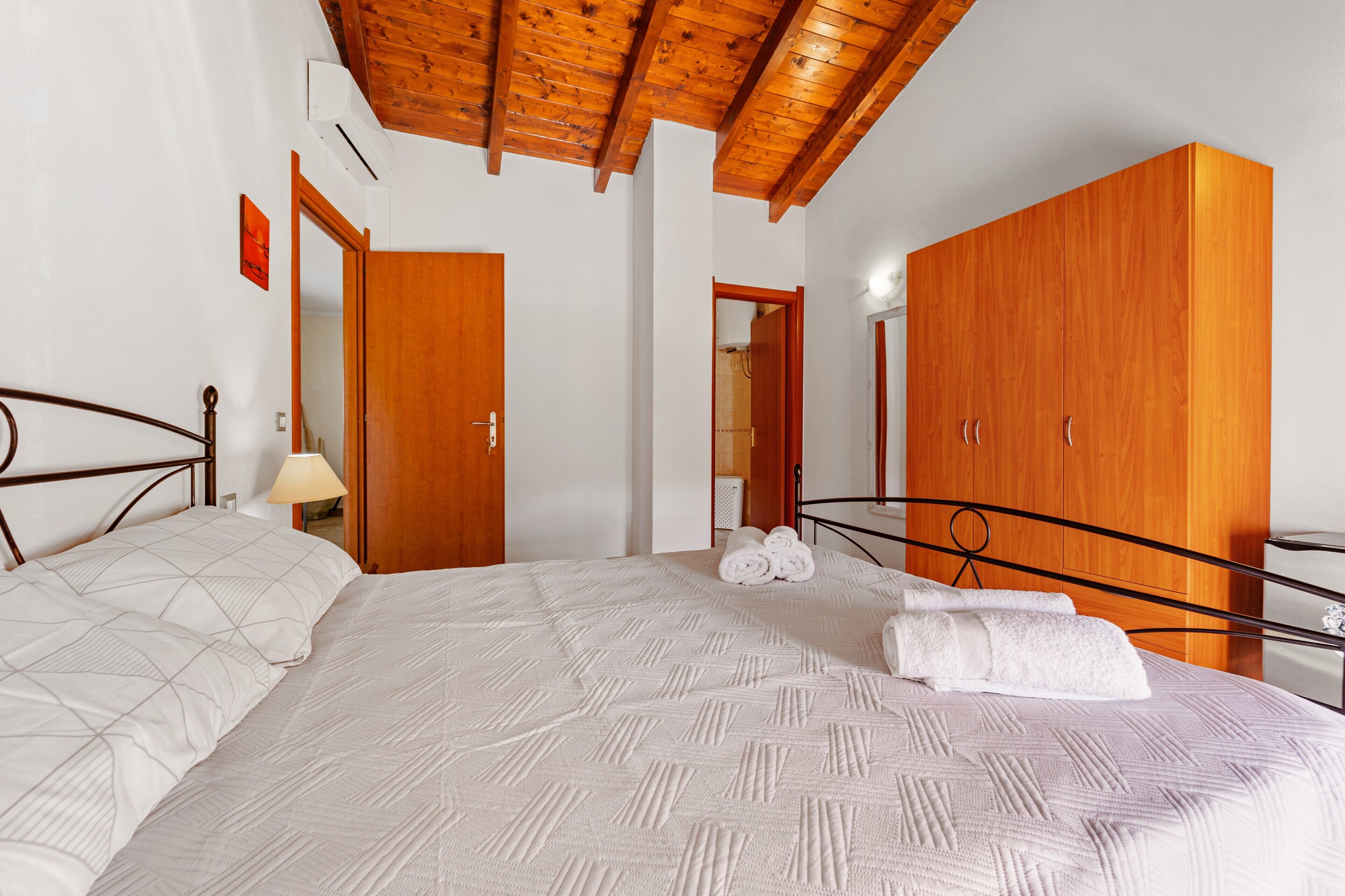 Une chambre à coucher avec un lit, une armoire en bois et un plafond avec des poutres apparentes.