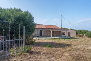 A stone house with a tiled roof, a fenced yard, and a clear sky.