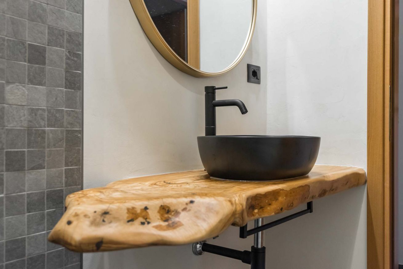 A bathroom with a wooden vanity, a black sink, and a gold-framed mirror.