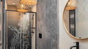 Une salle de bain moderne avec une douche à parois de verre, un lavabo noir et un miroir rond doté d’un cadre noir.