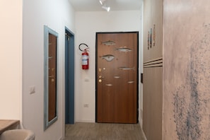 A hallway with a wooden door, a fire extinguisher, and a blue-framed mirror.