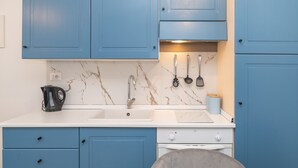 A kitchen with blue cabinets, a white countertop, a sink, a stove, and a kettle.