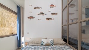 A bedroom with a bed, a wall with fish decals, a window with curtains, and a nightstand with a lamp.