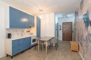 A compact kitchen with blue cabinets, a wooden dining table, and a small stool.