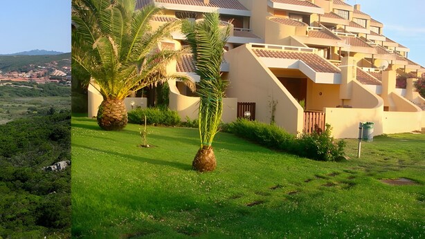 A coastal landscape with a beach, greenery, and a modern building with balconies.