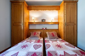 Une chambre avec deux lits, une tête de lit en bois, des lampes fixées au mur et une petite horloge sur l’étagère.