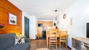 A cozy living room with a sofa, a dining table with chairs, a wooden coffee table, and a kitchen area with wooden cabinets and appliances.