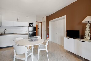 A modern kitchen with white cabinets, a dining table with chairs, a television on a cabinet, and a fire extinguisher.