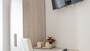 A hotel room with a wooden wardrobe, a small table with a tray of items, and a mounted TV.