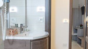 A modern bathroom with a large mirror, a white sink, and a wooden vanity.