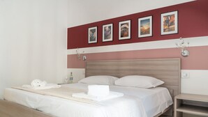 A modern hotel room with a large bed, white linens, a wooden headboard, and a wall with framed artwork.
