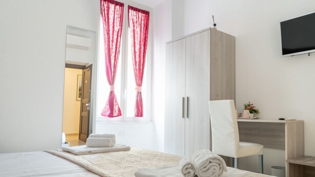 A hotel room with a bed, a desk, a chair, a wardrobe, and a TV on the wall.