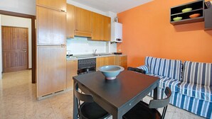 Une cuisine de taille réduite avec des meubles en bois, une table à manger avec des chaises, un bol bleu posé sur la table et un canapé à rayures adossé à un mur orange.