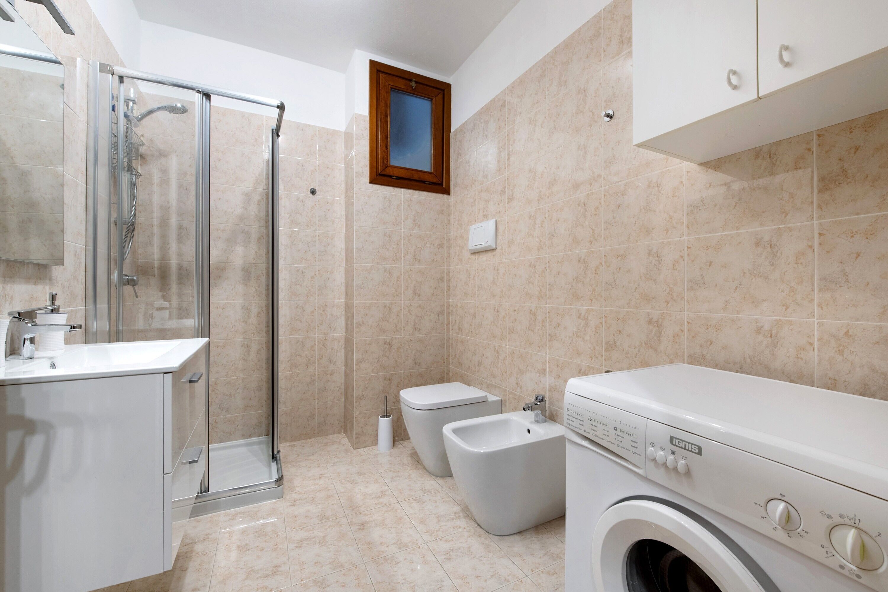 Ein Badezimmer mit Duschkabine aus Glas, Toilette, Bidet und einer Frontlader-Waschmaschine.