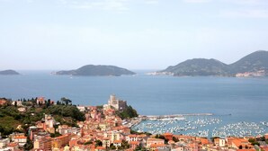 Un poble costaner amb edificis històrics, un port esportiu i un castell imponent a la vora d'un turó.