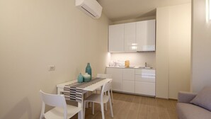 Cuina compacta amb armaris blancs, taula petita amb cadires i forn encastrat.