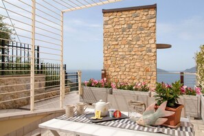 A terrace with a stone wall, a table with tea set, and a view of the sea.