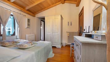 Un dormitorio con techo de madera, una cama con almohadones estampados, un armario, un radiador y un tocador con espejo.
